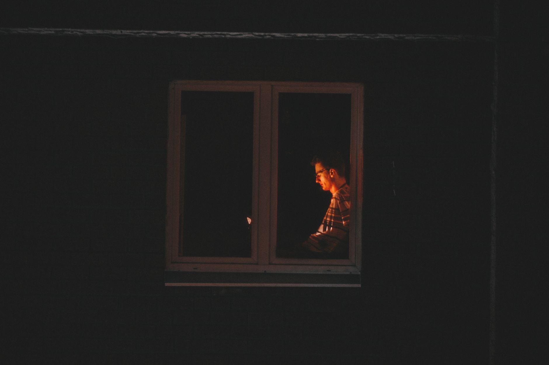 Silhouetted man working late at night in quiet solitude by window light.